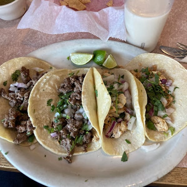 Four Carmela's Mexican Restaurant tacos, two with beef and two with chicken, garnished with cilantro and onions.