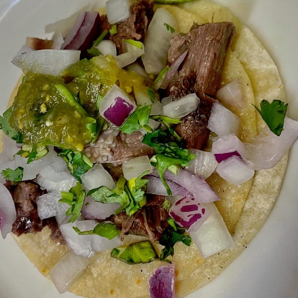 Close-up of a Carmela's Mexican Restaurant taco with meat, green salsa, white and red onions, and cilantro.